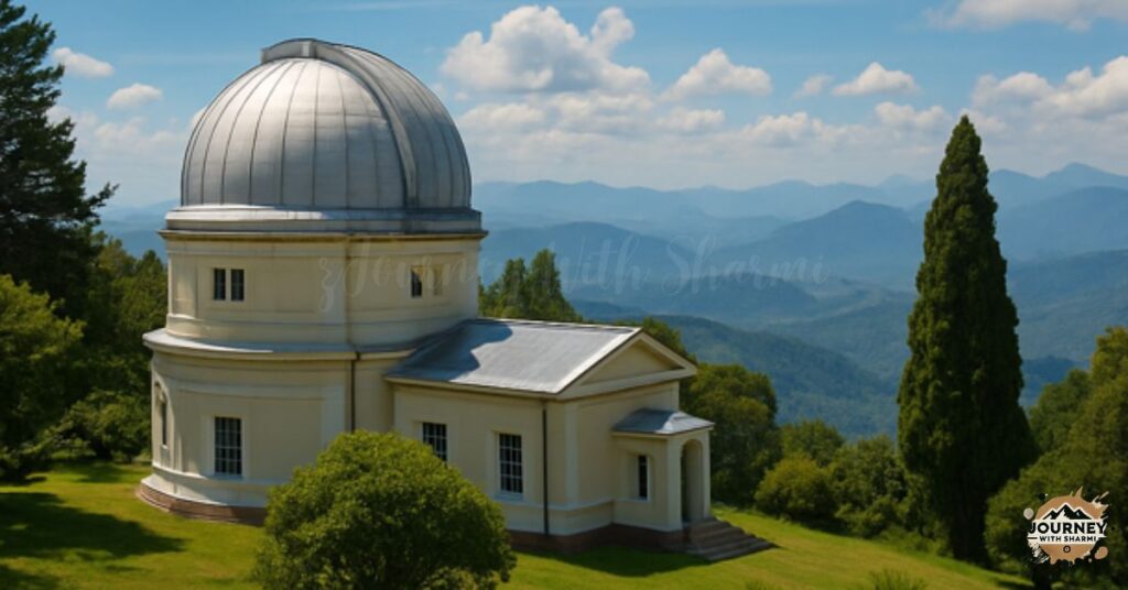 Kodaikanal Solar Observatory in Tamil Nadu, featuring a white dome-shaped building on a grassy hilltop, surrounded by lush greenery and panoramic views of the Western Ghats under a bright blue sky.